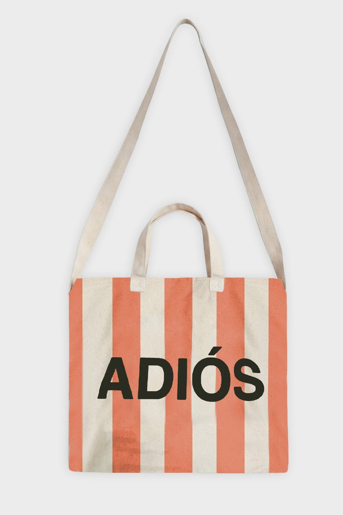 A canvas tote bag with vertical coral orange and cream stripes, featuring the word 'ADIÓS' printed in bold black letters across the front. It has two cream fabric shoulder straps and two short top handles, shown against a plain light gray background.