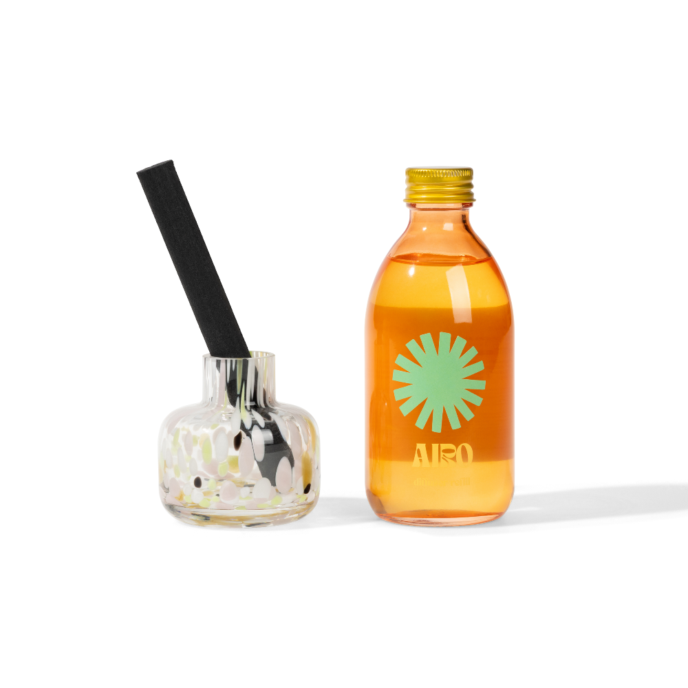 Orange bottle airo room diffuser with a green logo and black straw next to a small glass container on a white background