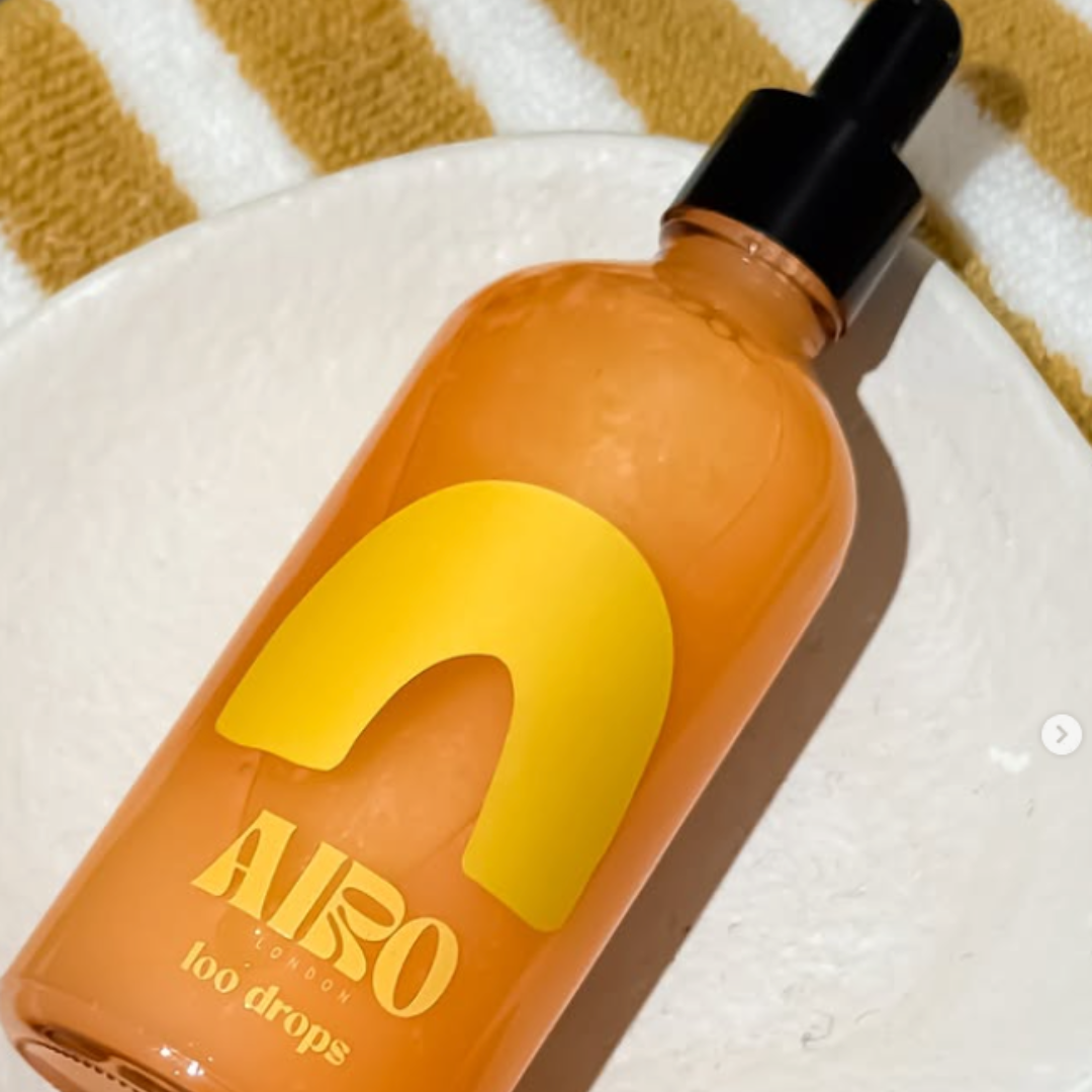 Orange bottle with yellow cap labelled 'Airo' loo drops scented on a striped fabric background