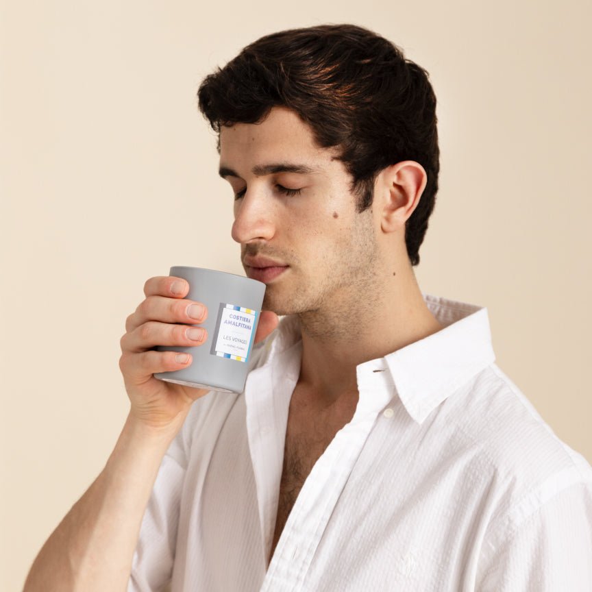 Man holding a grey candle with a label against a beige background