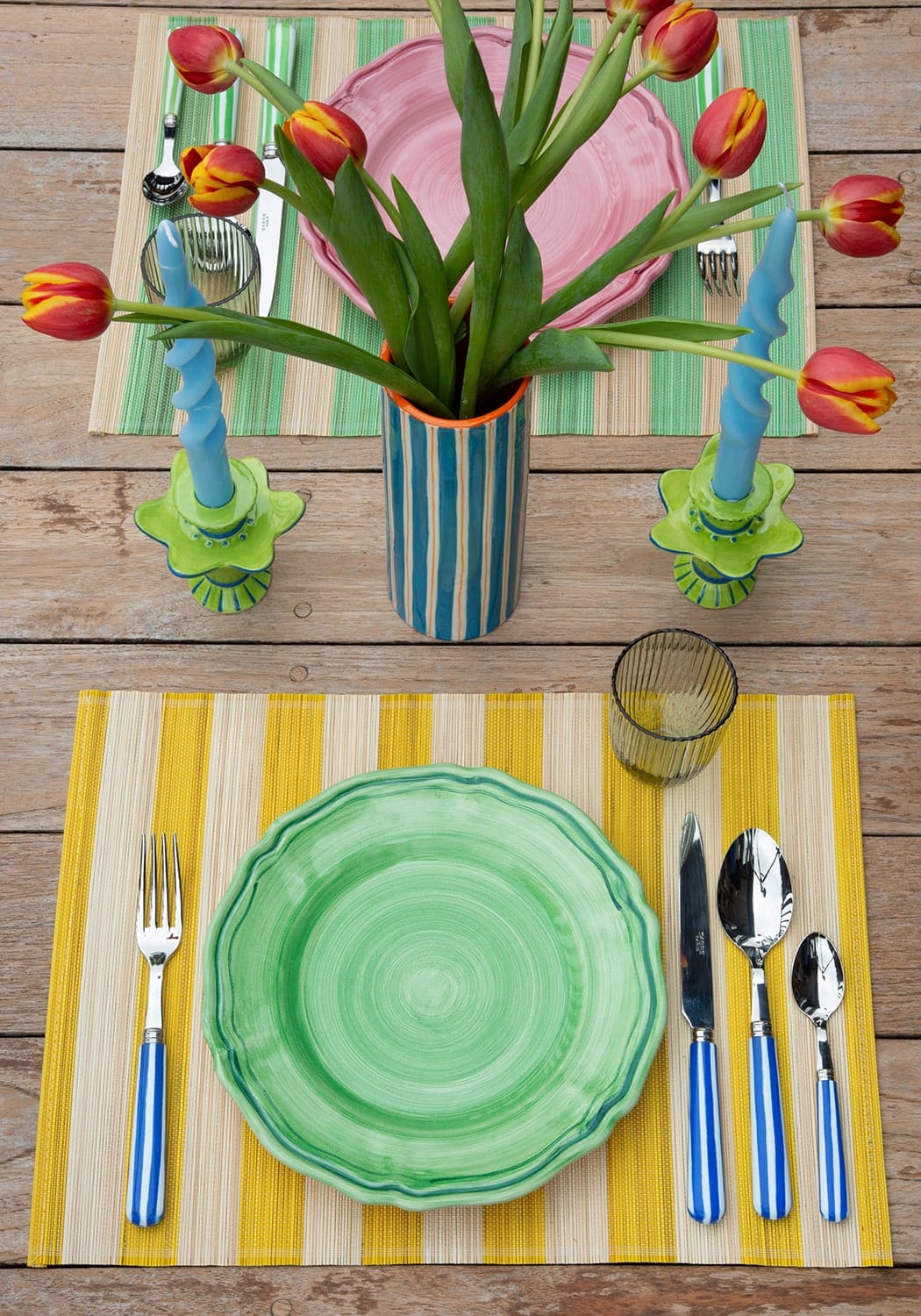 Colourful table setting with tulips, striped placemats, and patterned plates on a wooden table.