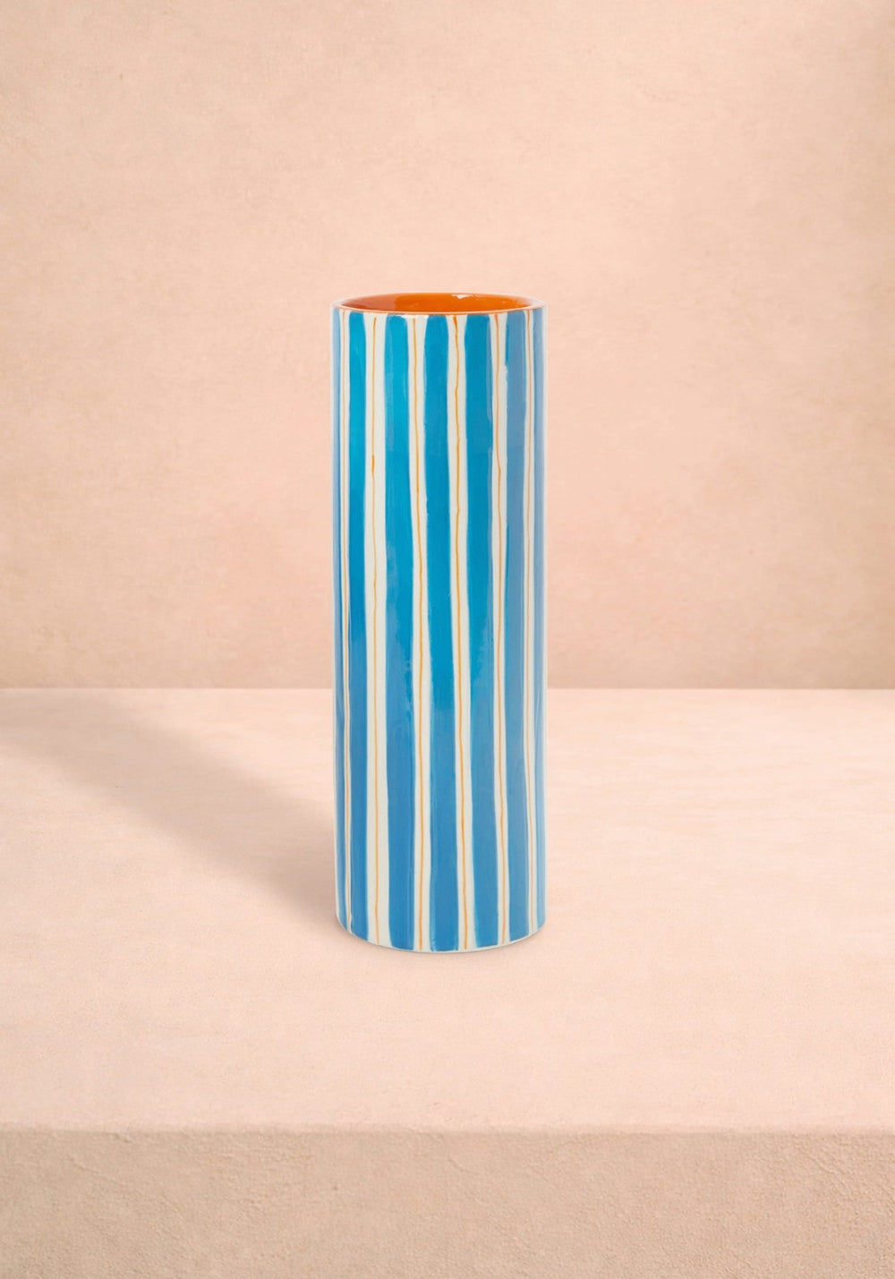 Tall cylindrical vase with blue white and orange striped pattern on a beige background