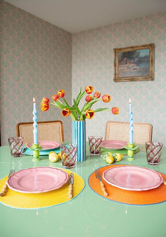 Dining table set with colorful plates, placemats, and tulips in a room with patterned walls.