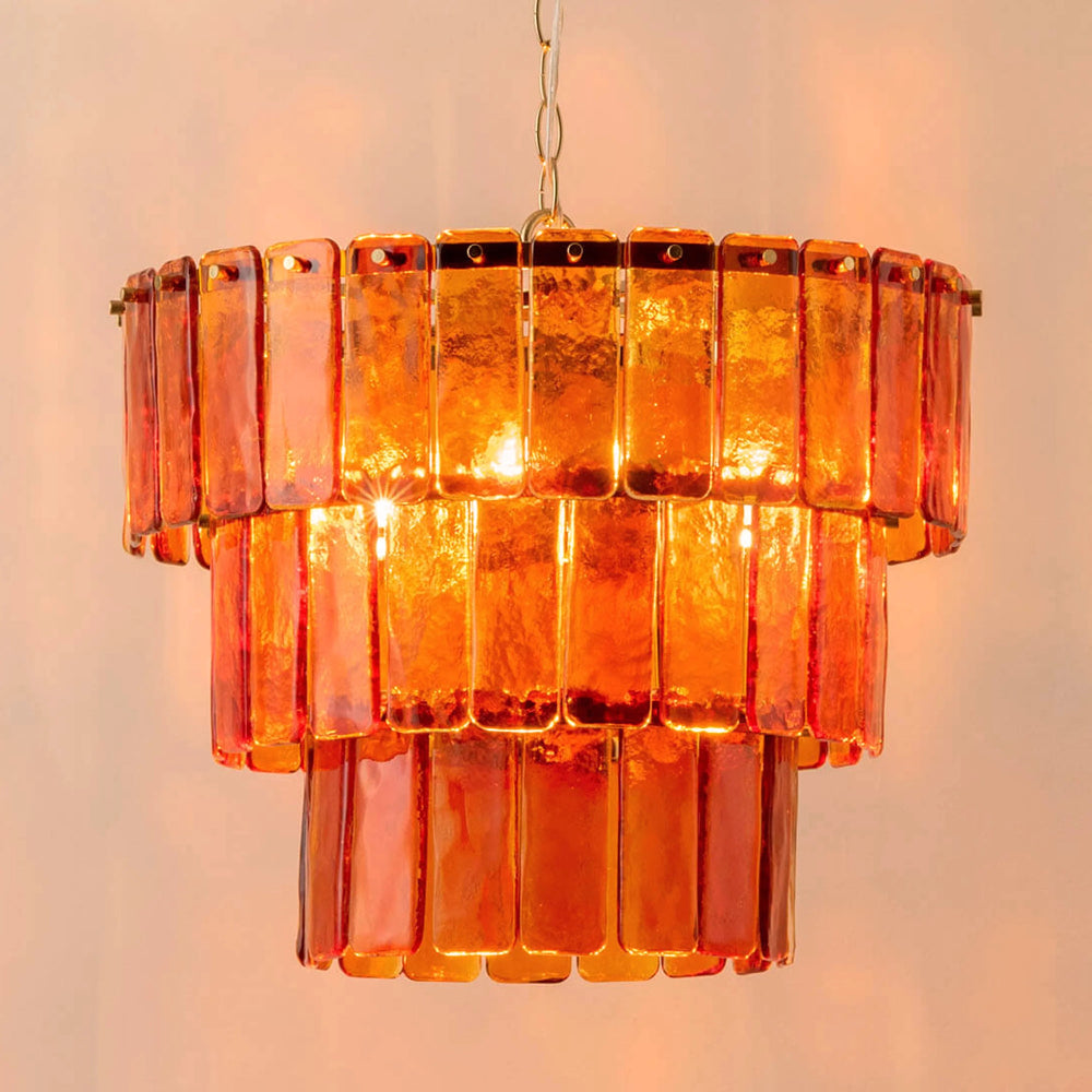 Lit view of amber glass chandelier with brass frame