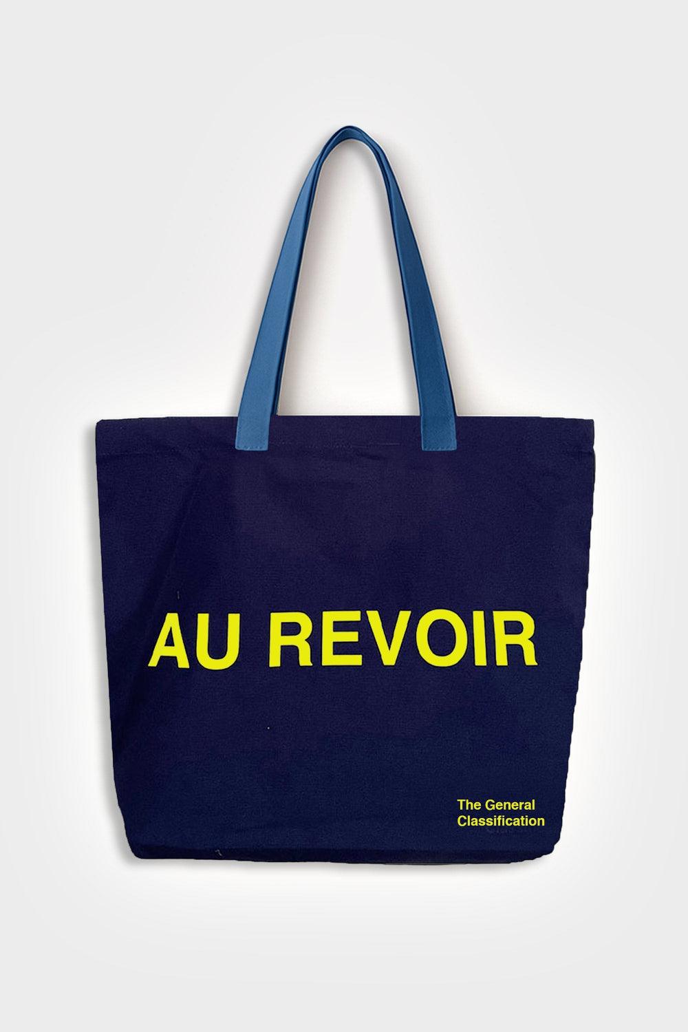 A navy blue canvas tote bag with blue handles, featuring the text 'AU REVOIR' in bold yellow letters across the front, and 'The General Classification' printed in small yellow text in the bottom right corner, set against a light grey background.