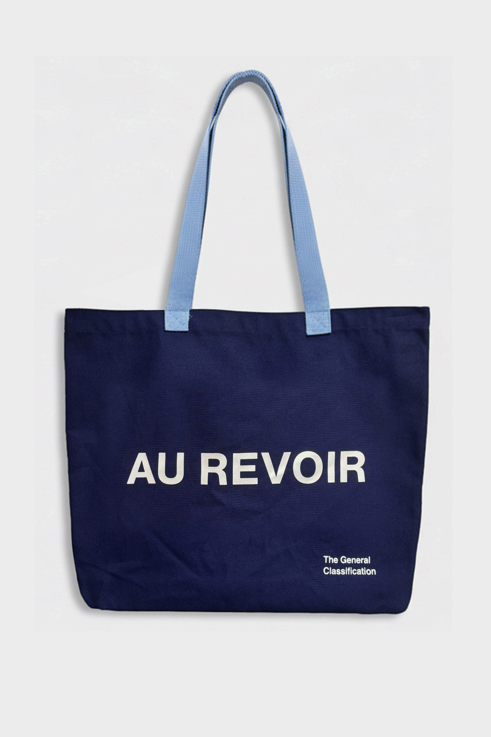 A navy blue canvas tote bag with light blue shoulder straps and white printed text reading 'AU REVOIR' on the front, photographed against a plain light grey background.