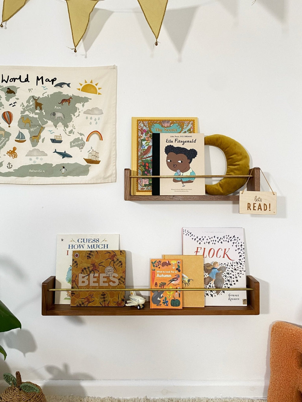 Children's books on a shelf with a world map poster on a white wall.