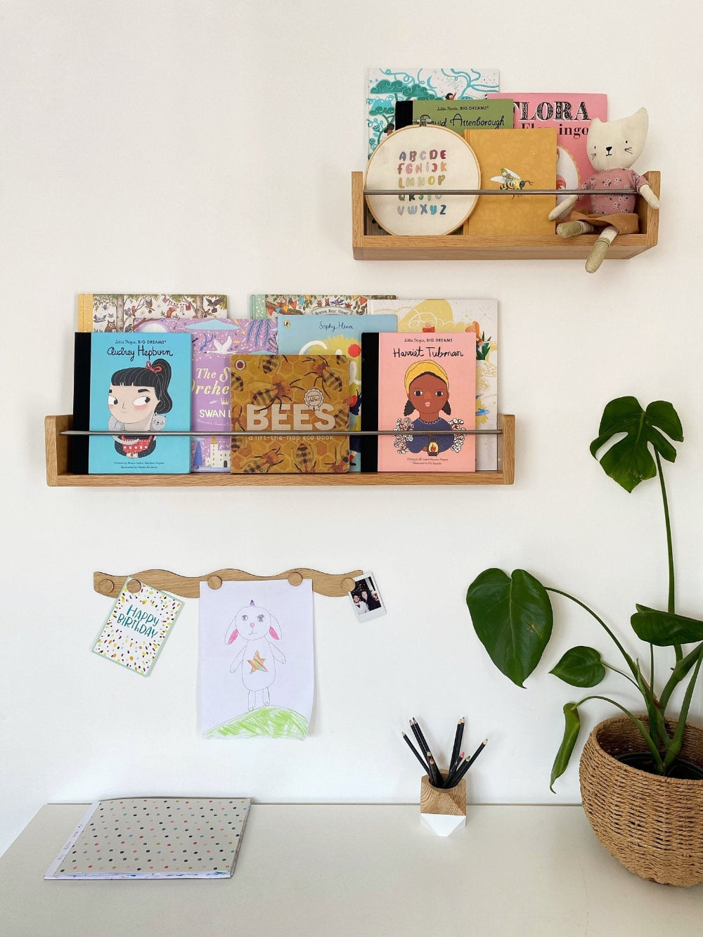 Wooden shelves with books and stationery on a white wall, next to a plant.