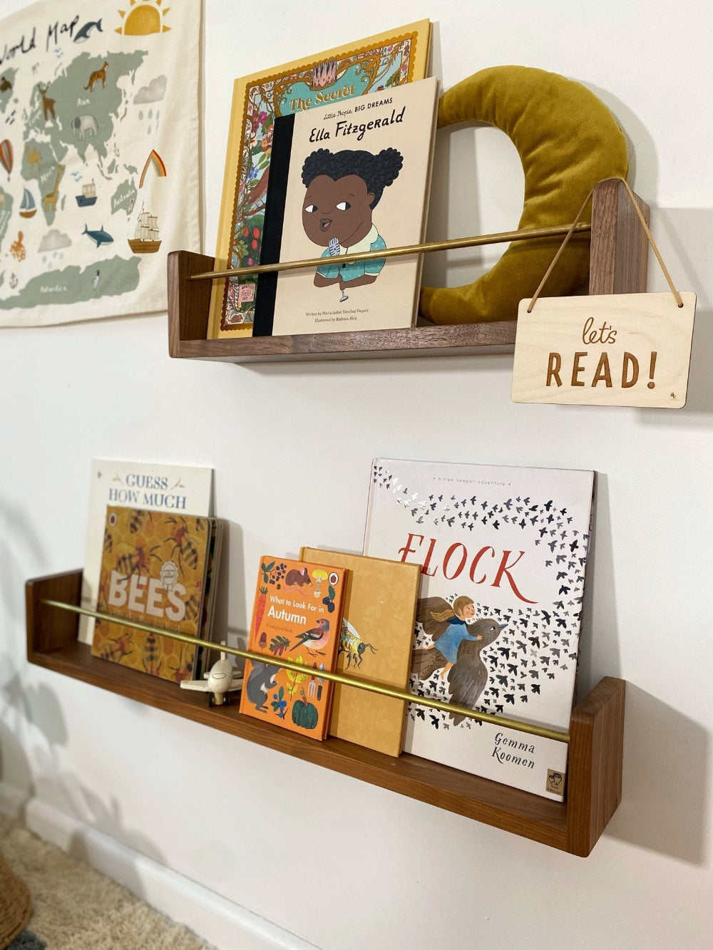 Children's books on a wooden shelf with a decorative sign that says 'let's READ!' against a white wall.
