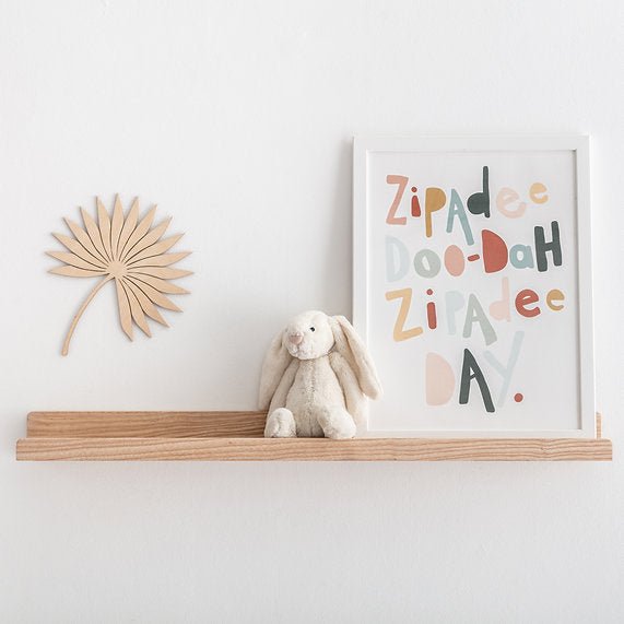 Wooden shelf with a plush toy and decorative wall art on a white wall.