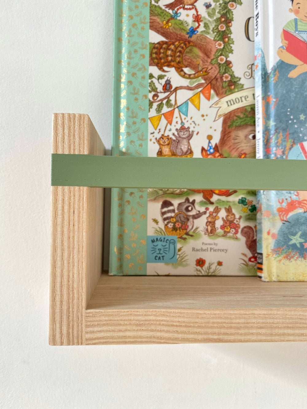 Children's books with colourful book covers on a wooden shelf with a green holder.