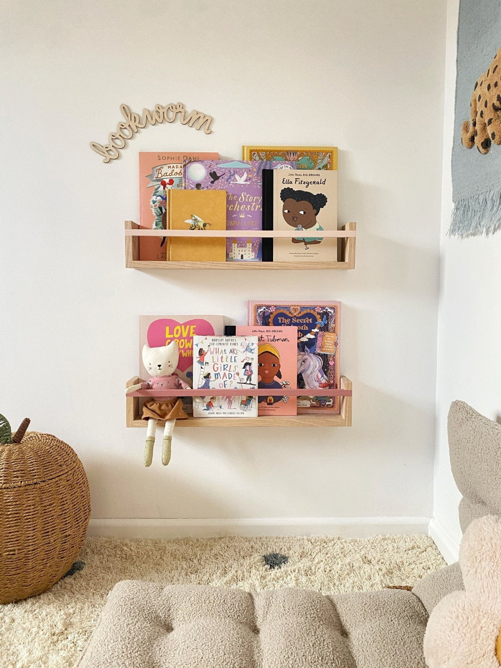 Wooden shelves with children's books on a white wall, with a soft rug and toy in the foreground.