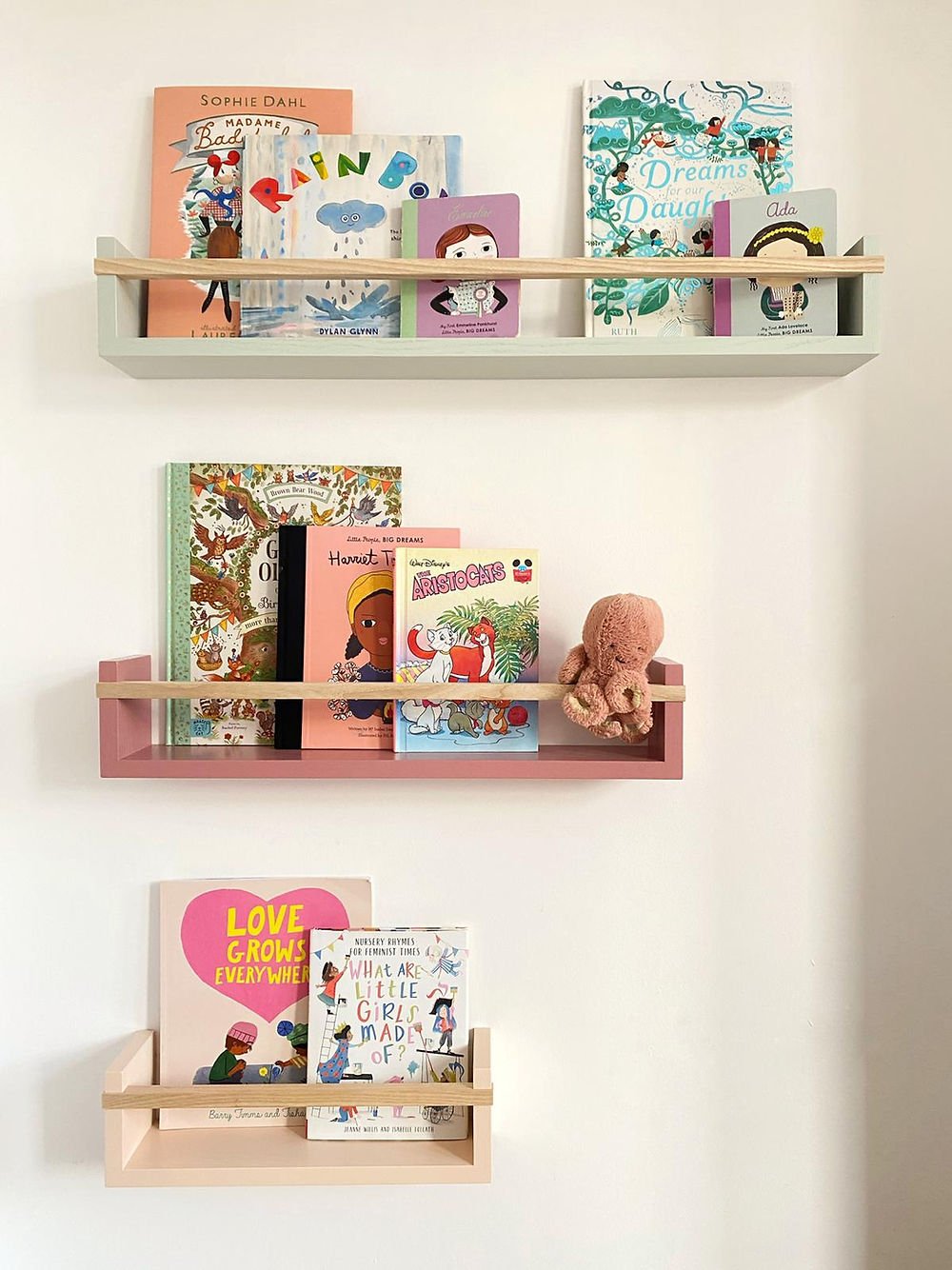 Children's books and toys on wooden shelves against a white wall