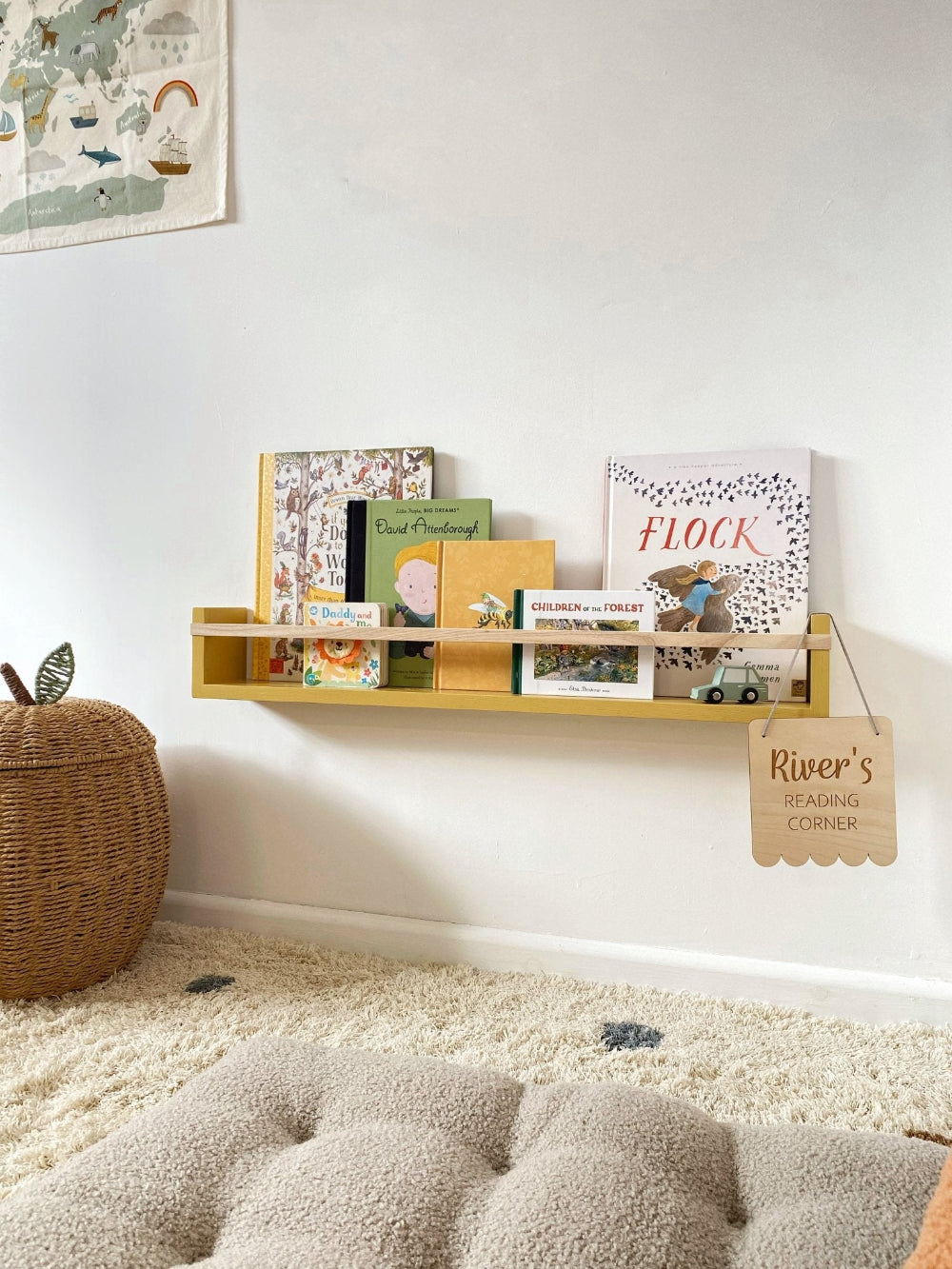 Wooden shelf with books and decor items against a white wall, with a textured rug and wicker basket in the foreground.