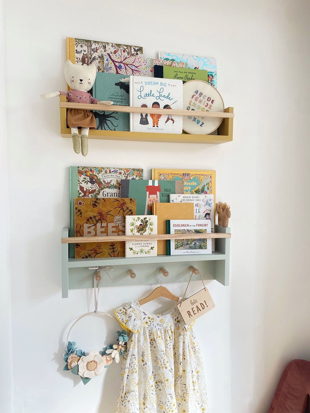 Wall-mounted shelves with books, toys, and a dress in a child's room.