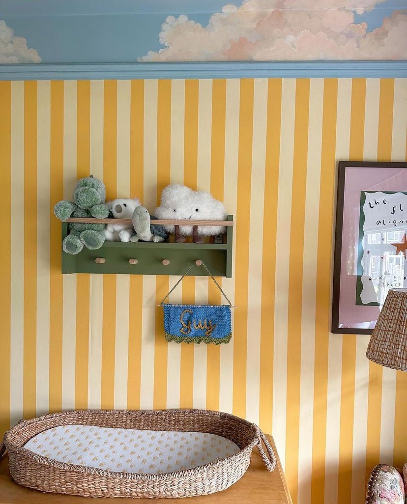 Children's room with yellow and white striped walls, a green shelf with toys, and a wicker basket on the floor.