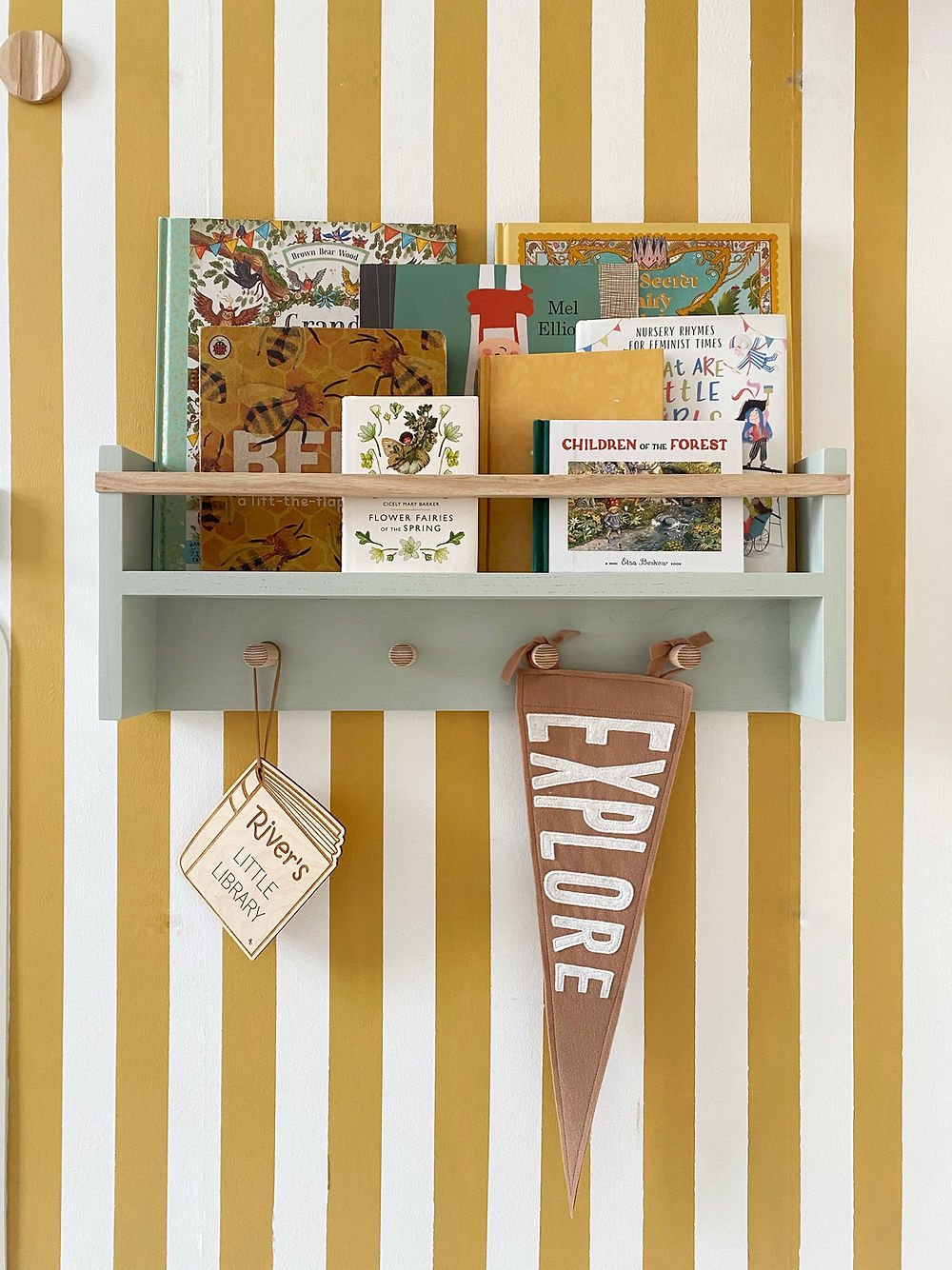 Children's books and a pennant on a shelf against a striped wall.