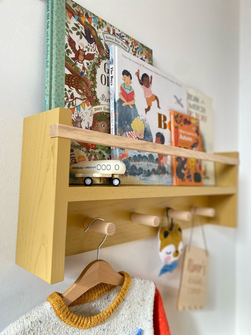 Wooden shelf with books, a toy car, and a hanger on a white wall.