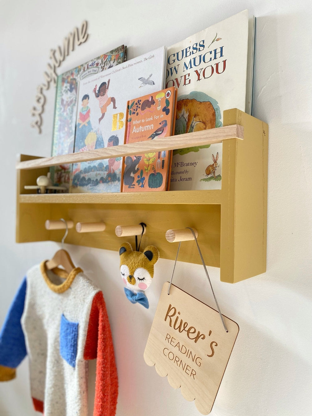 Wooden shelf with children's books and a tag reading 'River's Reading Corner' on a white wall.