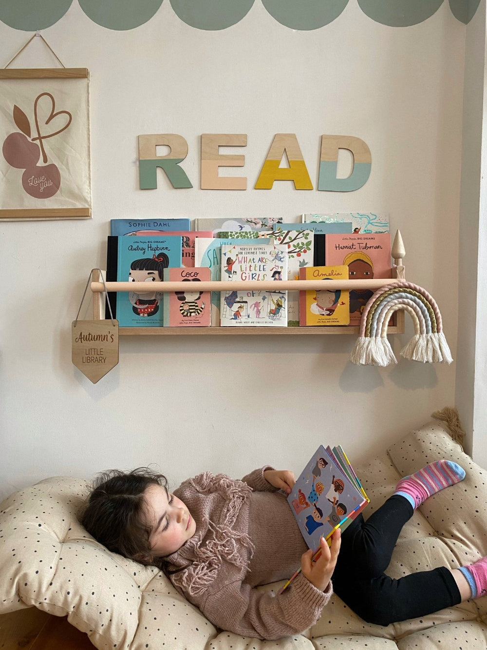 Child reading a book on a couch with a wall display of books and 'READ' sign.