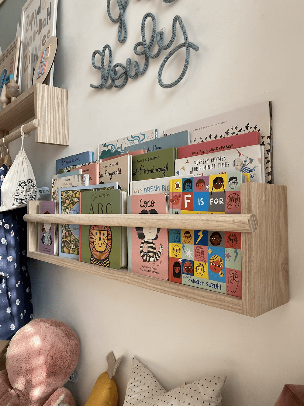 Children's books on a wooden shelf with decorative elements on a wall.
