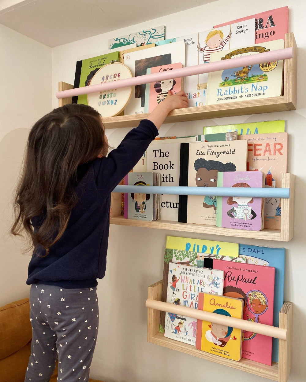 Child reaching for a book on a wall-mounted children's bookshelf filled with books.