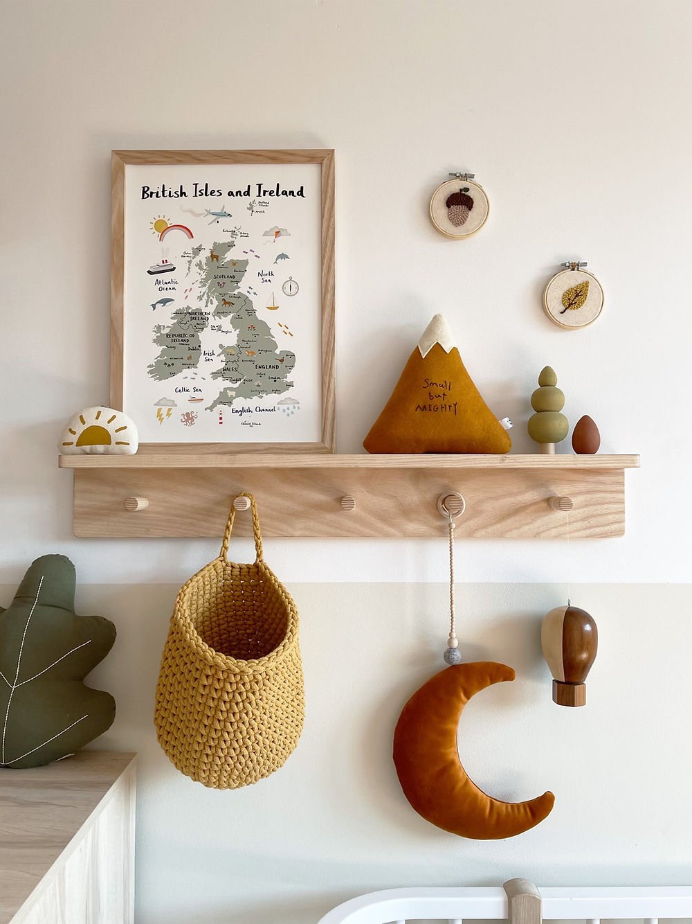 Wooden shelf with decorative items including a framed map, plush toys, and hanging baskets against a light wall.