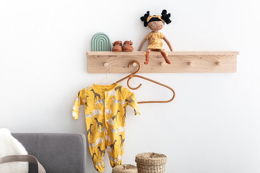 Yellow baby onesie with animal print hanging on a wooden shelf with a doll and shoes.