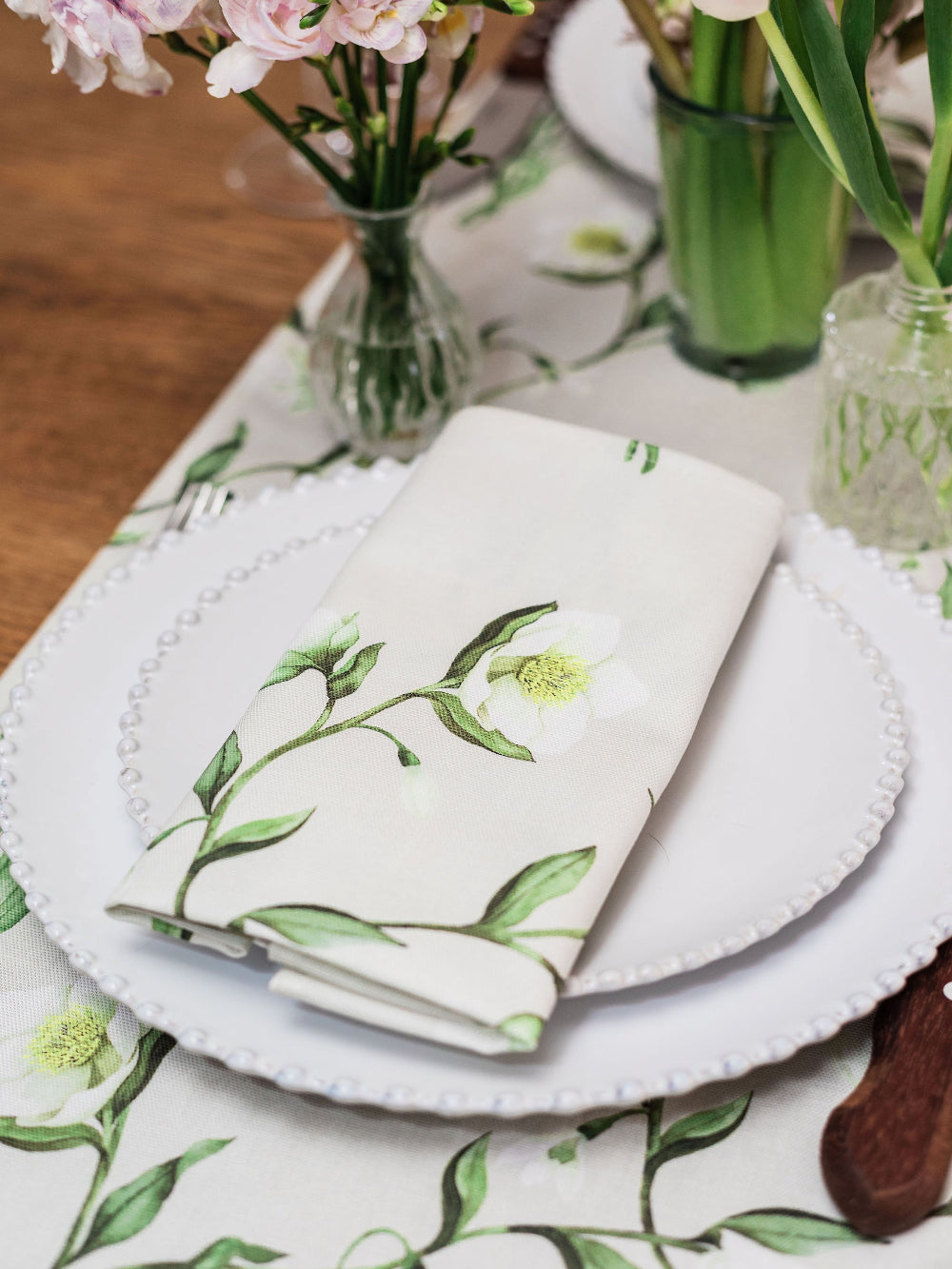 Table setting with floral-patterned napkin and placemat, accompanied by flowers in vases.