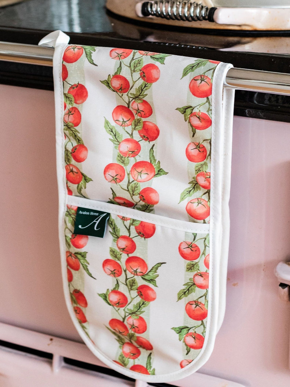 Oven mitt with tomato vine pattern hanging on a stove handle