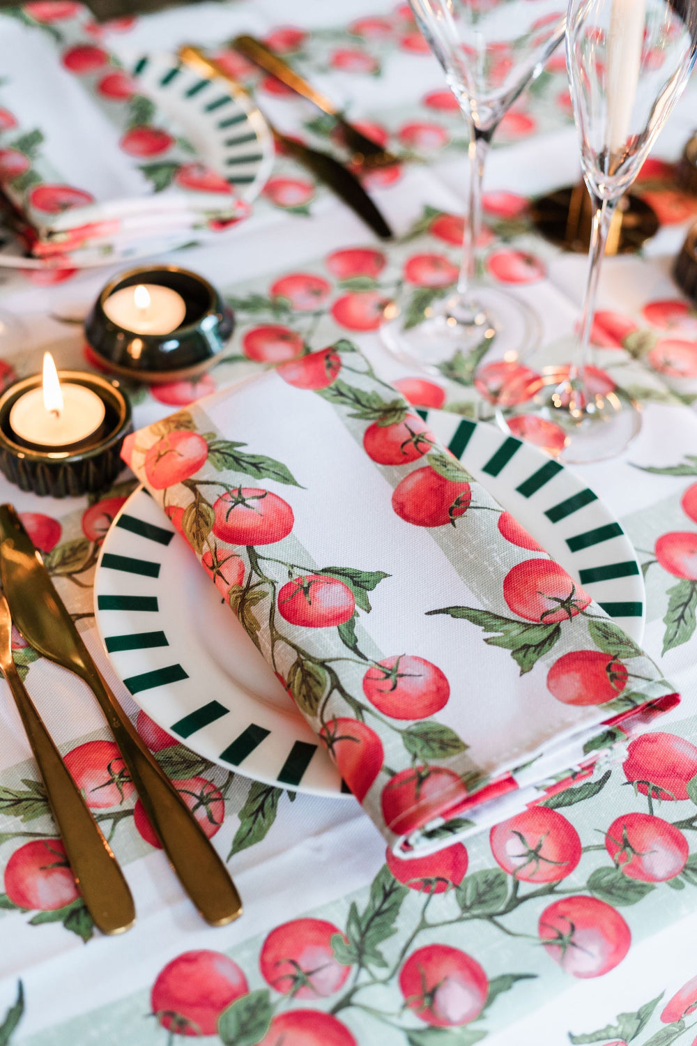 Dining table setting with tomato-patterned tablecloth, plates, and napkins.