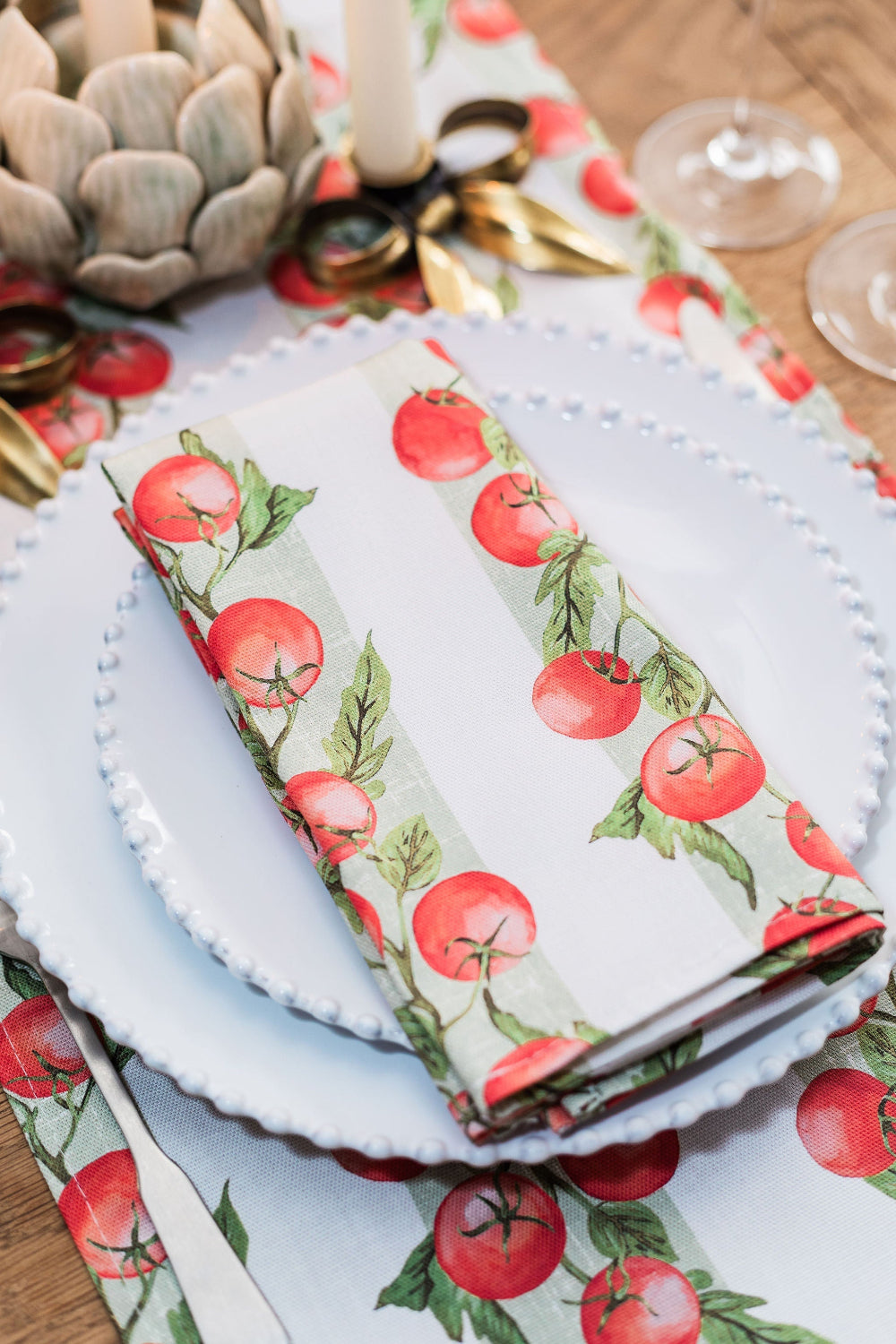 Table setting with tomato-patterned napkin and placemats on a wooden table.
