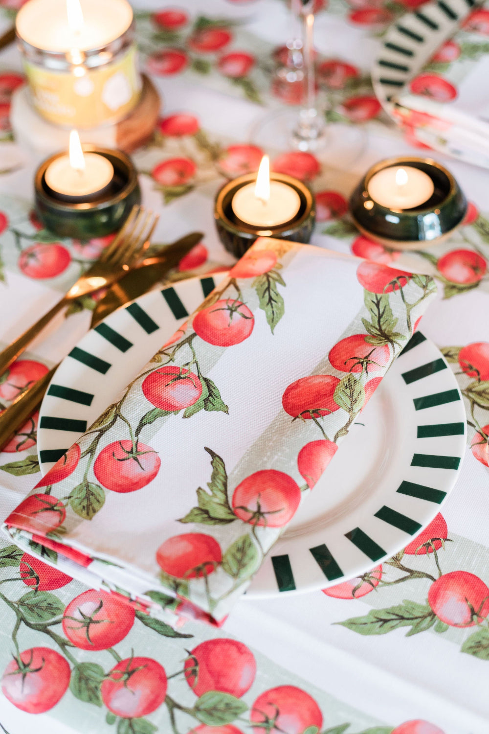 Table setting with floral-patterned plates, tomato napkins, and candles on a matching tablecloth.