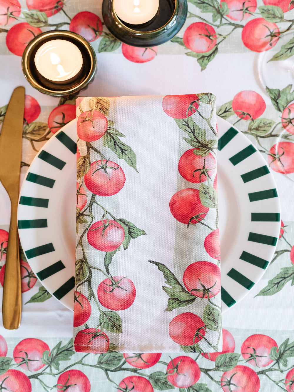 Dinner setting with ceramic plates, tomato vine napkin, and candles on a tablecloth with tomato pattern