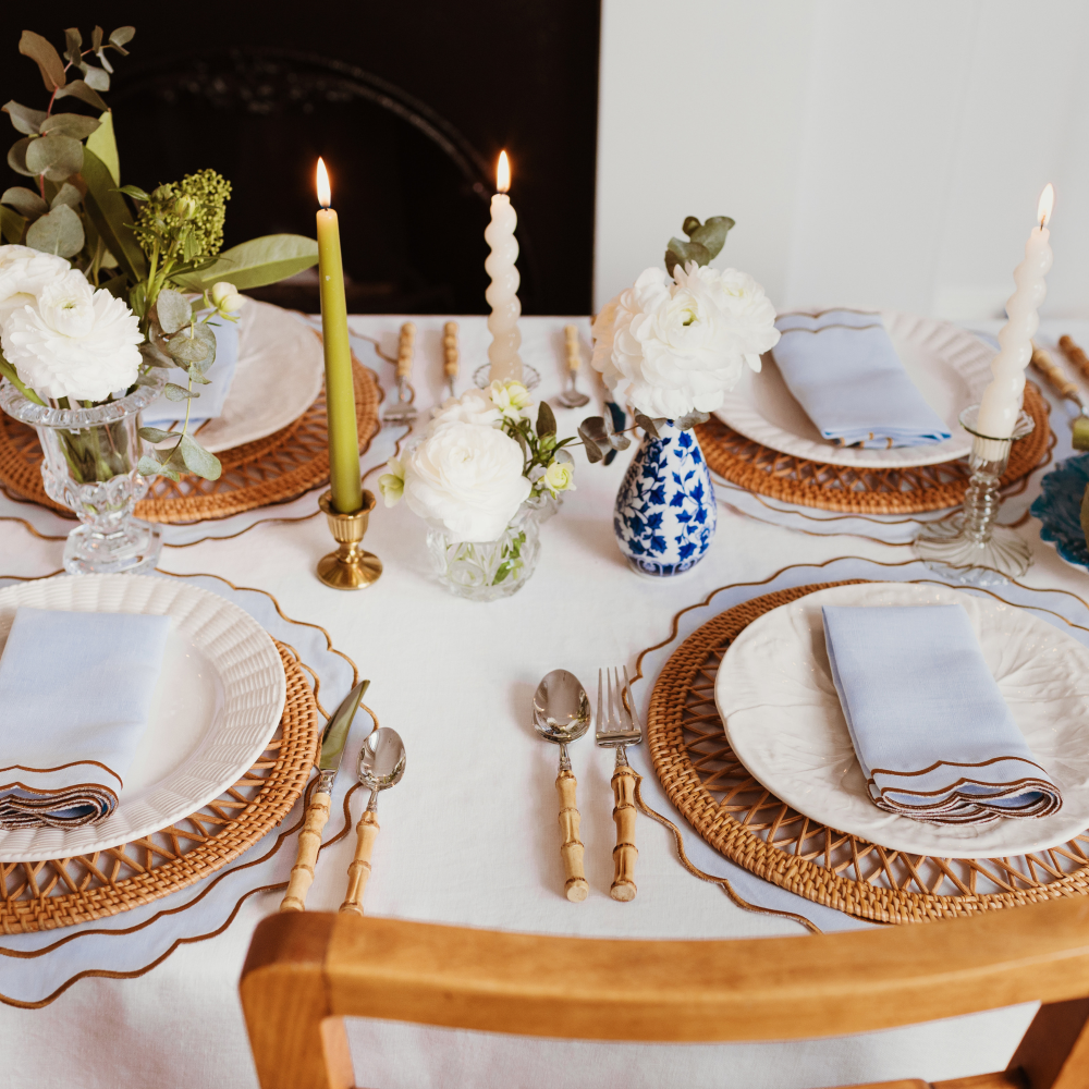 Elegant table setting with white tablecloth, wicker chargers, candles, and floral arrangements.