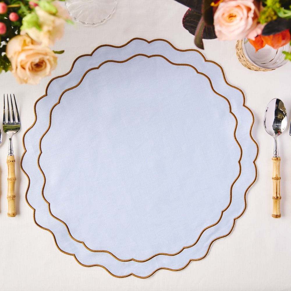 Light blue placemat with gold rim on a table setting with flowers and cutlery.