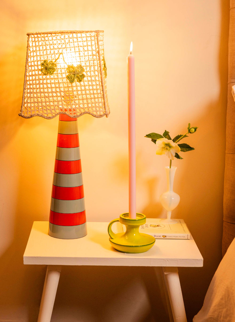 Decorative lamp with striped design on a small table with metre candle against a warm-toned wall.