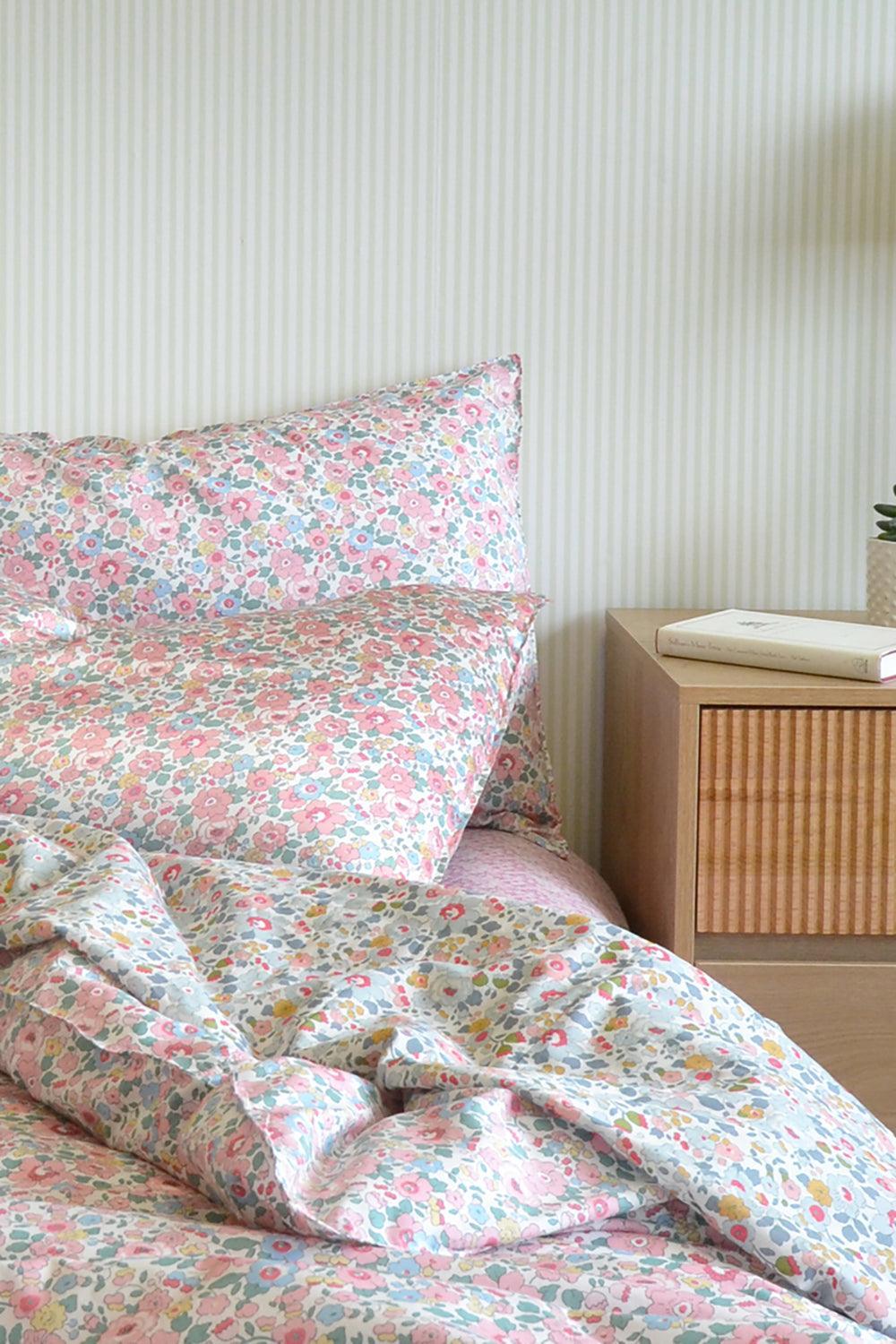 Floral bedding set on a bed with a wooden nightstand in the background.