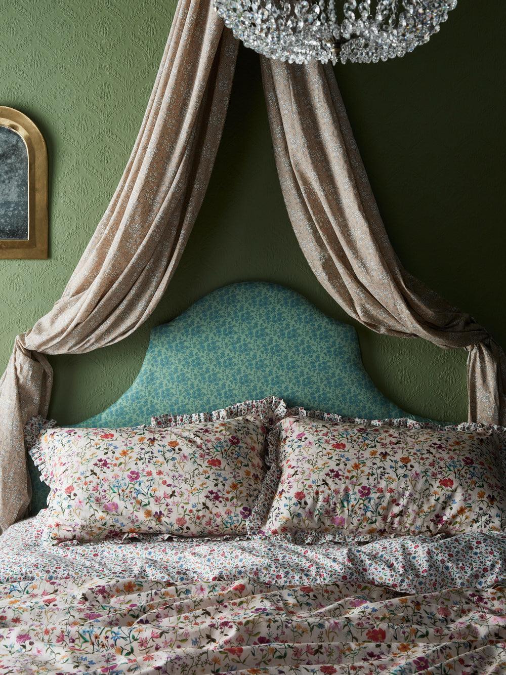 Floral bedding on a bed with draped curtains against a green wall.