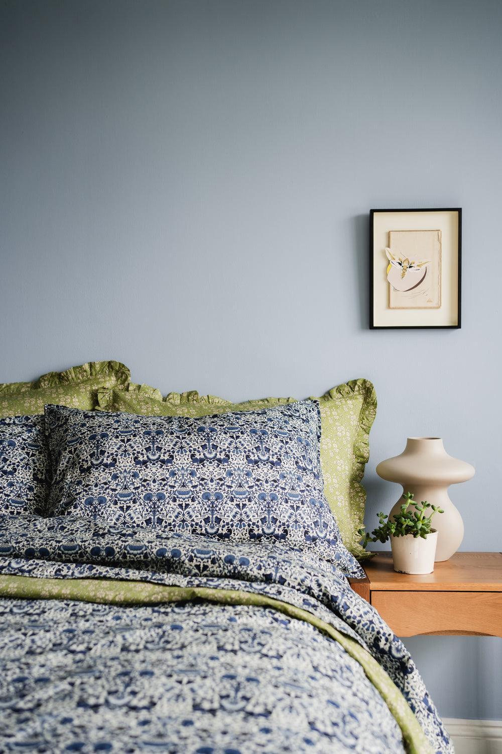 Bed with floral bedding and green pillows against a gray wall with a framed picture.