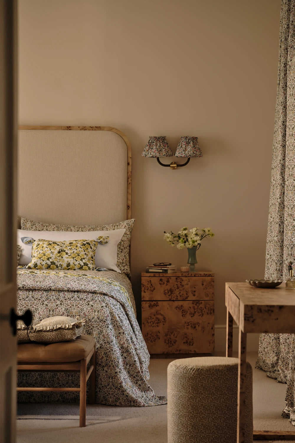 Cozy bedroom with floral bedding, wooden nightstand, and wall lamp.