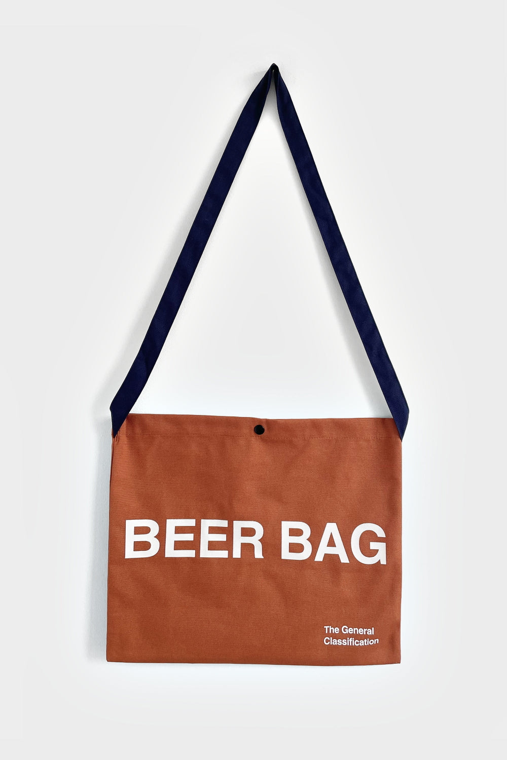 A brown canvas shoulder bag with a navy blue strap, featuring the words 'BEER BAG' printed in white on the front, with a small logo reading 'The General Classification' below it.