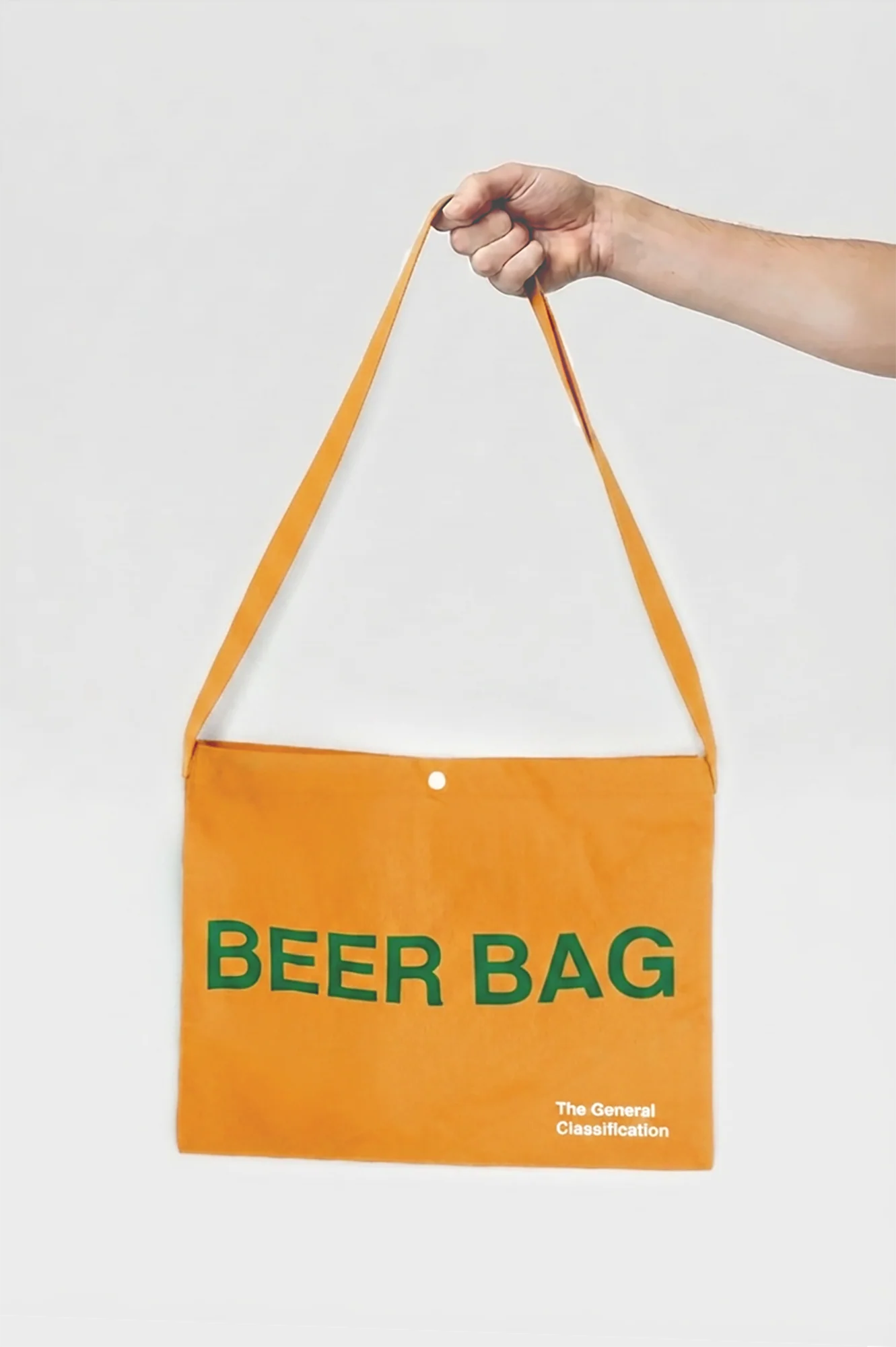 An orange canvas shoulder bag with green text reading 'BEER BAG' and small white text reading 'The General Classification' in the bottom right corner, held by a person's hand against a light gray background.