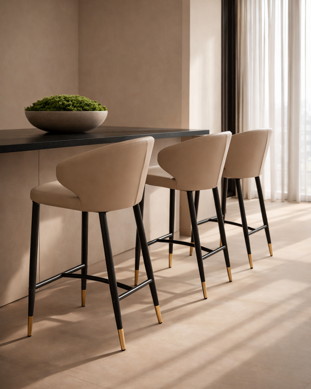 Three beige bar stools with black legs and gold feet around a kitchen island.