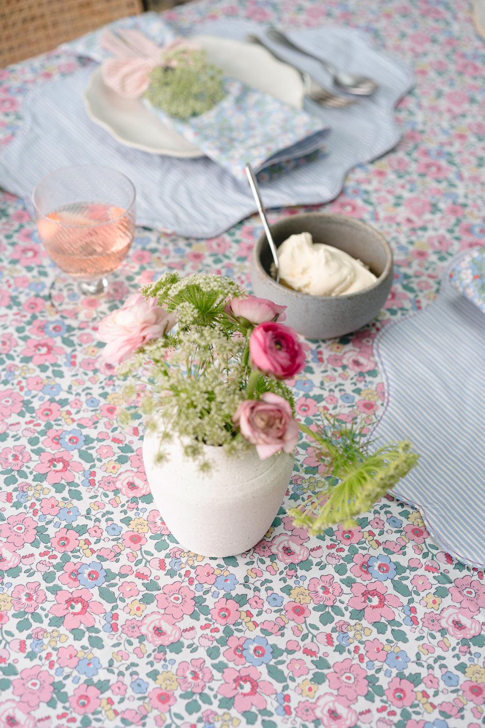 Table setting with floral tablecloth, flowers in a vase, and a bowl of cream.
