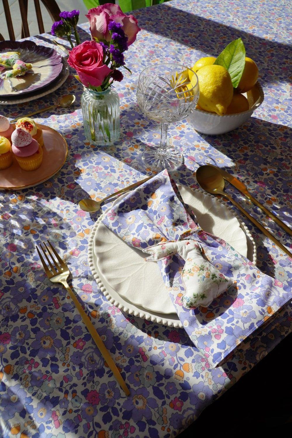 Dining table setting with floral tablecloth, plates, cutlery, and decorative items.