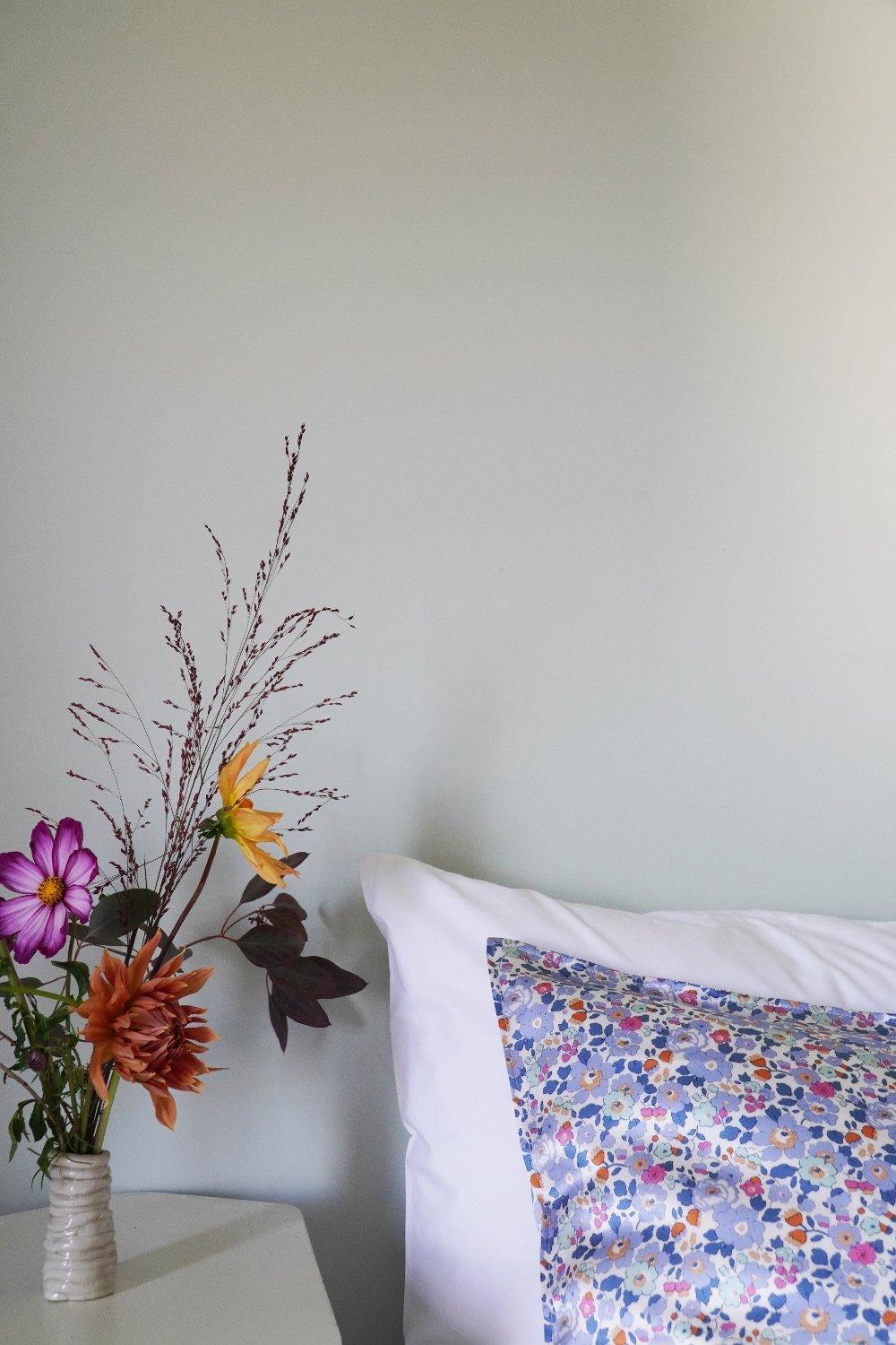 Floral arrangement in a vase next to a pillow with a floral pattern on a light-coloured surface.