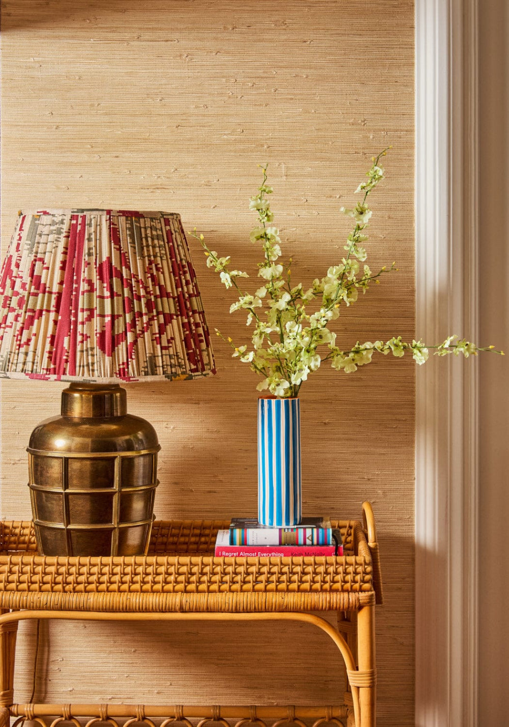 Decorative lamp with plaid shade and brass base on a wooden side table against a bamboo wall.