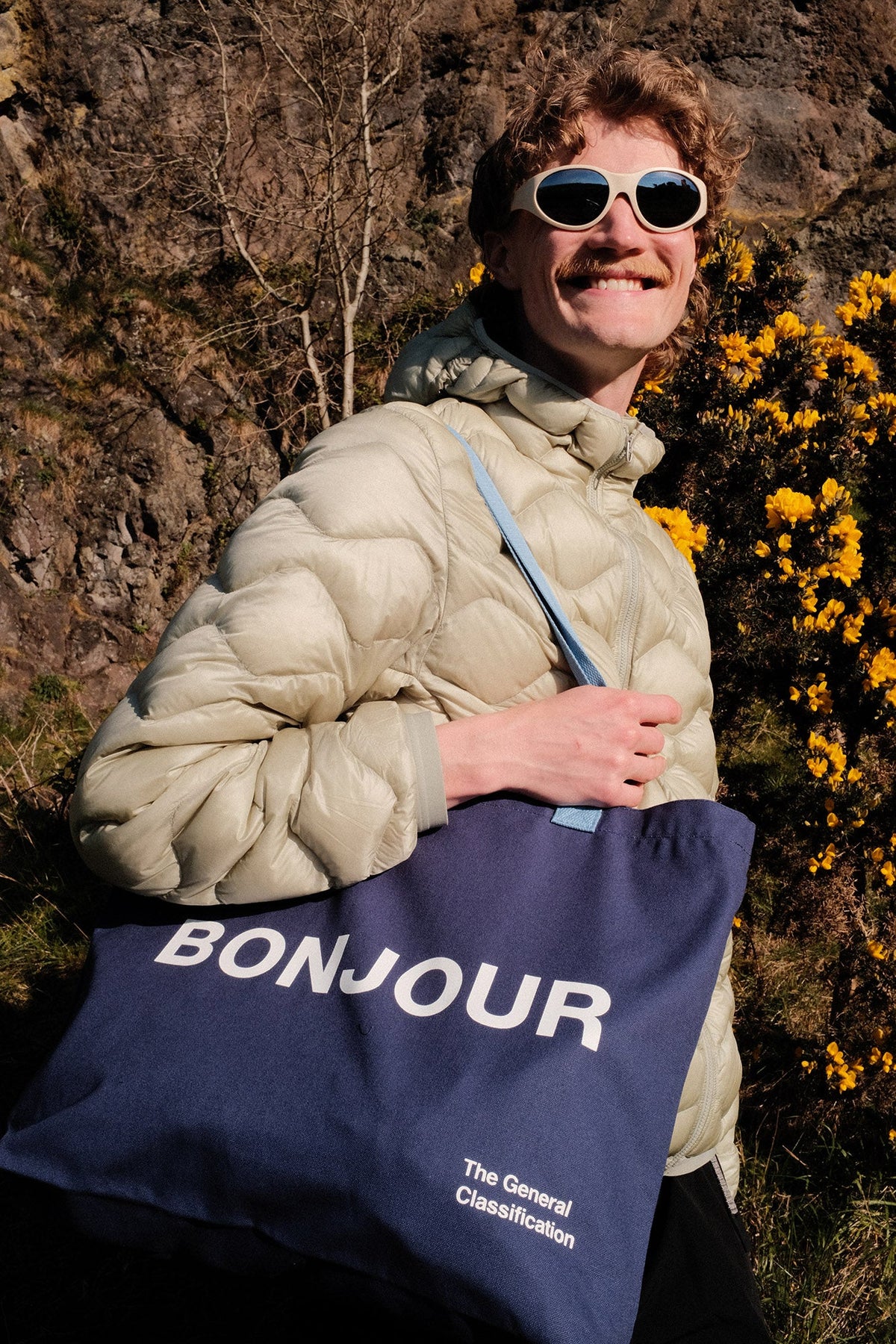 Person holding a blue tote bag with 'Bonjour' text against a natural background