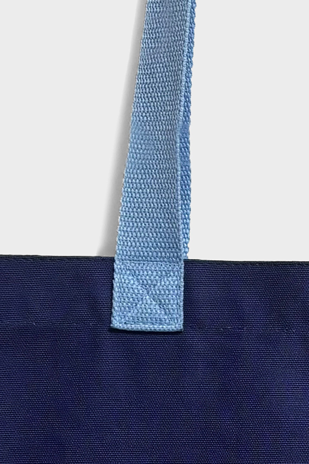 Close-up of a navy blue fabric tote bag with a light blue woven handle against a light grey background.